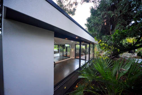 White rendered exterior and dark-framed glazing beside the garden