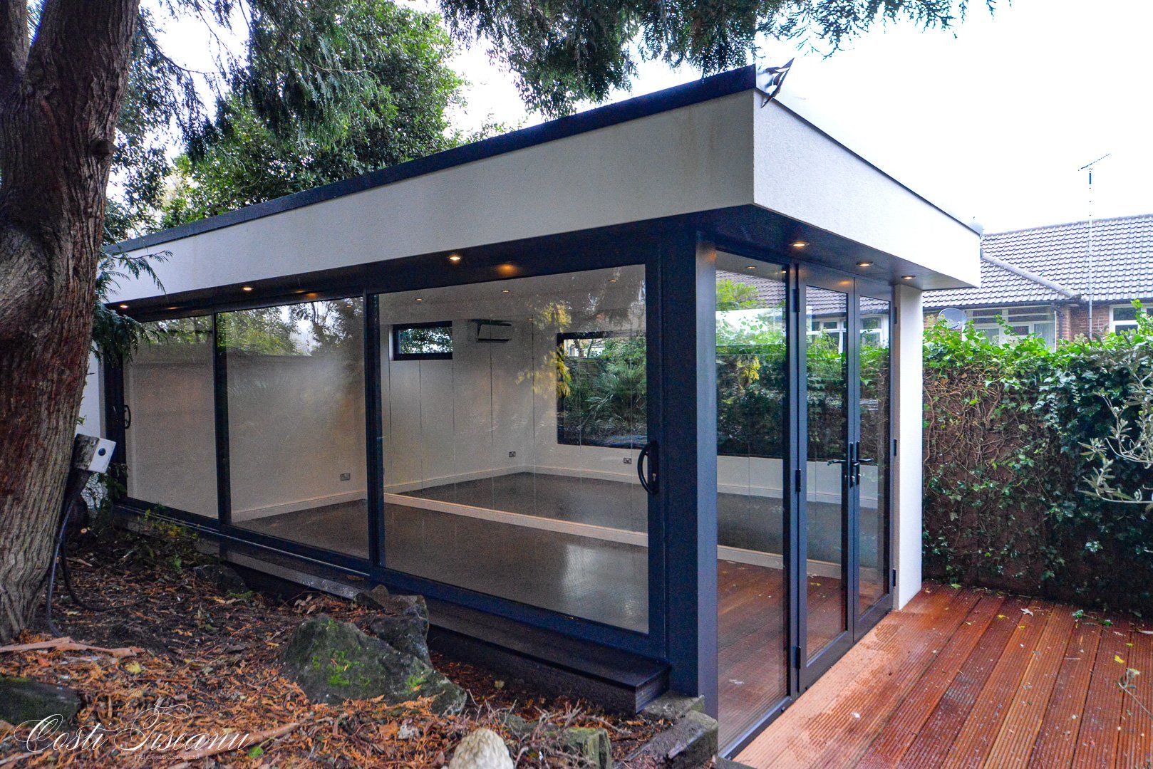 Glazed garden building with a flat roof and timber deck
